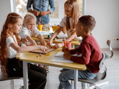 Happy kids using wooden geoboard at primary school with teacher on the background